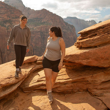 Two people walking on a rocky outcrop with a canyon background