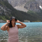 girl wearing a rose colored organic cotton tank top standing next to a lake and mountains