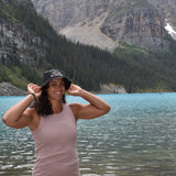girl wearing a rose colored organic cotton tank top standing next to a lake and mountains