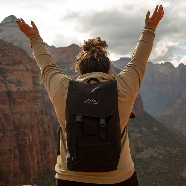 Person with a recycled polyester backpack standing on a mountain top with arms raised towards the sky